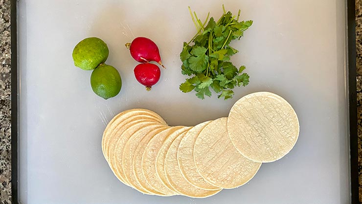 Tortillas, limes, jalapeno peppers, and cilantro on a cutting board