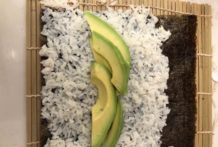 White rice, avocado slices, and seaweed wrap on a bamboo mat